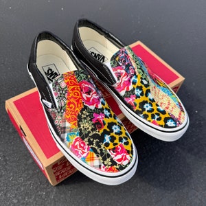 May include: A pair of black slip-on Vans shoes with a colorful patchwork design featuring flowers, paisley, and animal print. The shoes have white soles and black laces.