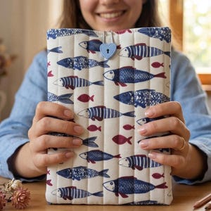 Può includere: Copertina per libri trapuntata con un motivo a pesci blu navy e rossi su sfondo crema. Chiusura con un lucchetto a forma di cuore azzurro. Il design presenta varie illustrazioni di pesci e piccoli pesci rossi.