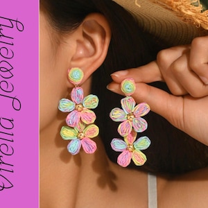 Könnte beinhalten: Mehrfarbige Blumenohrringe im Pastell-Regenbogen-Design. Die Ohrringe haben drei Blumenschichten und einen runden Aufsatz mit goldfarbenen Akzenten. Der Text "Virella Jewelry" befindet sich auf einem lila Hintergrund.