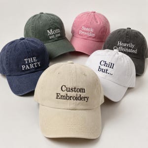 May include: Six baseball caps in shades like navy, pink, and khaki. Each cap has embroidered text, including "The Party," "Mom," and "Custom Embroidery." The caps have a classic, casual design, suitable for everyday wear.