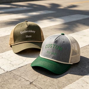 May include: Two trucker caps with mesh backs. One is olive green with "Embroidery Here" embroidered in white. The other is grey with a green brim and "CUSTOM EST 2020" embroidered in green. Both have a rope detail.