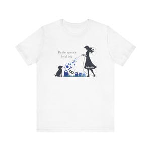 以下が含まれることがあります： グラフィックデザインの白いTシャツ。犬につながれたリードを持っている女性のシルエットが描かれています。デザインには「Be the queen's loyal dog」というテキストとブランド名「kokokin」が含まれています。犬は草の上に座っています。