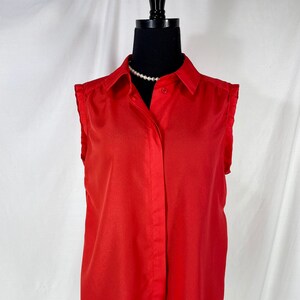 May include: A red sleeveless button-down shirt with a collared neckline. The shirt has a slightly ruffled trim on the shoulders.