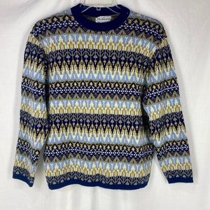 May include: A blue, white, and gold patterned sweater with a crew neck. The sweater has a geometric design and is made of a soft, knitted fabric.