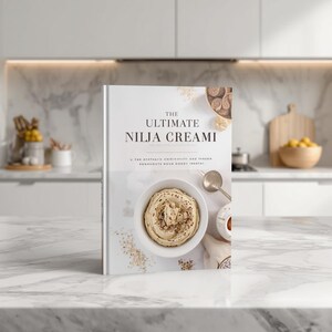 May include: A hardback cookbook titled The Ultimate Nilja Creami with a white cover featuring a central image of a bowl of creamy dessert, a silver spoon, and scattered ingredients. The text is printed in black, centred on the front cover.
