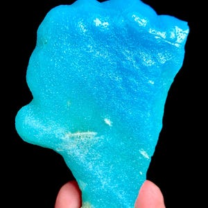 Könnte beinhalten: Ein rohes, leuchtend blaues Mineralexemplar mit einer durchscheinenden, kristallinen Textur und einer unregelmäßigen, organischen Form. Die Oberfläche zeigt eine Mischung aus hellen Cyan- und tieferen Azurtönen mit rauen Kanten.
