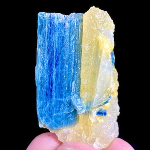 Op de afbeelding: Een ruw mineraal exemplaar met een verticale scheiding tussen een diepblauw, gestreept kristallijn gedeelte en een doorschijnend, lichtgeel, getextureerd kristallijn gedeelte. De structuur is langwerpig met scherpe, grillige randen en lagen.