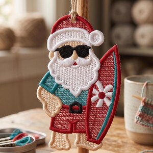 May include: Embroidered Santa Claus ornament wearing sunglasses and holding a surfboard. The ornament features a red Santa hat, shorts, and surfboard with a white flower design. The Santa has a white beard and is wearing a blue shirt.