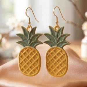 May include: A pair of gold-toned pineapple earrings. The earrings feature a yellow, textured pineapple body with green leaves. The earrings hang from gold-colored hooks.