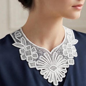 Puede incluir: Un cuello de encaje blanco con un intrincado patrón floral y geométrico con un gran motivo central similar a una margarita, superpuesto sobre una prenda de color azul marino oscuro. El encaje presenta detalles de calados y bordes.