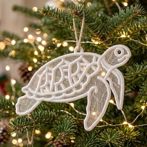 May include: A white lace sea turtle ornament featuring an intricate openwork mesh pattern and a solid stitched border. The sea turtle is suspended by a thin tan twine loop, showcasing a detailed shell design and flippers in a flat, lightweight construction.