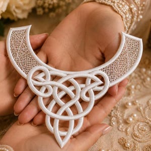 May include: A white lace collar applique featuring an intricate, interconnected knotwork pattern. The design includes a curved upper section with a fine mesh texture and a central, elaborate woven motif that extends downward into a pointed shape.