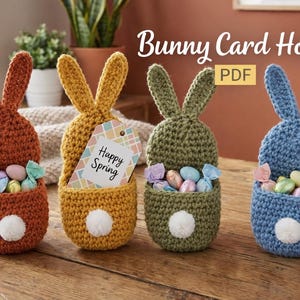 May include: Four crocheted bunny-shaped card holders in orange, yellow, green, and blue, each with a white pom-pom tail and a pocket filled with wrapped candies. The yellow bunny holds a tag that says "Happy Spring".