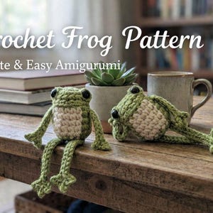 May include: Two crocheted frog amigurumi, one sitting and one lying down, on a wooden table. The frogs are green and cream-colored, with black eyes. The text "Crochet Frog Pattern" and "Cute & Easy Amigurumi" are visible.