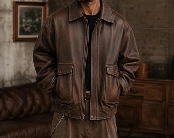 Könnte beinhalten: Eine braune Leder-Bomberjacke mit klassischem Kragen, durchgehendem Frontreißverschluss und zwei großen Pattentaschen auf der Vorderseite. Die Jacke hat einen gerippten Saum und Bündchen sowie ein durchgehendes, abgenutztes Finish.