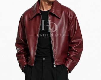 Könnte beinhalten: Eine dunkelburgunderrote Lederjacke mit breitem Kragen, langen Ärmeln und einem silberfarbenen Frontreißverschluss. Auf der Brust ist der Text HD LEATHER HUB in Weiß aufgedruckt, getragen über einem schwarzen Oberteil und einer schwarzen Hose.