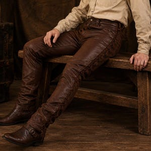 May include: Dark brown leather trousers featuring a decorative lace-up detail running down the outer side of each leg. The trousers have a fitted silhouette and are paired with dark brown leather boots that include a buckle strap across the ankle.