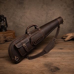 May include: A dark brown leather carrying case with a tapered shape, featuring a top handle, an adjustable shoulder strap, a buckled front pocket, and a smaller side pocket with multiple loops for small items, all secured with brass-toned hardware.