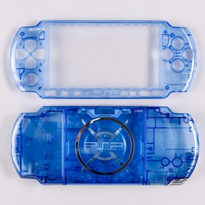 May include: A transparent blue PSP console shell, showcasing the front and back pieces. The Sony logo is visible on the top piece. The bottom piece features the UMD label and a circular design.