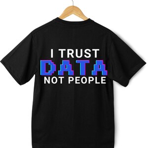 May include: Black t-shirt with the text "I TRUST DATA NOT PEOPLE" in white and pixelated blue and purple letters. The shirt is hanging on a wooden hanger against a white background.