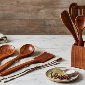 K&ouml;nnte beinhalten: Eine Sammlung von K&uuml;chenutensilien aus Holz, darunter L&ouml;ffel und Spatel, die auf einer Marmoroberfl&auml;che pr&auml;sentiert werden. Die Utensilien haben eine warme braune Farbe und sind mit einem Kupfertopf und einem kleinen Teller mit Gew&uuml;rzen angeordnet.