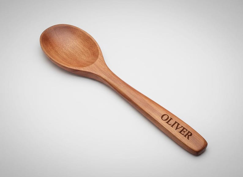 K&ouml;nnte beinhalten: Ein Holzl&ouml;ffel mit einem abgerundeten L&ouml;ffel und einem langen Griff. Der Griff ist mit dem Namen "OLIVER" graviert. Der L&ouml;ffel ist aus hellbraunem Holz gefertigt und wird wahrscheinlich zum Kochen oder Servieren verwendet.