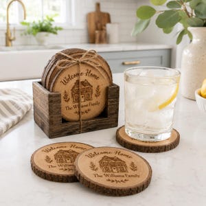 Könnte beinhalten: Ein Set aus Holzuntersetzern mit einem natürlichen, rustikalen Rand. Jeder Untersetzer ist mit "Welcome Home", einer Hausillustration und "The Williams Family" graviert. Die Untersetzer befinden sich in einem Holzhalter.
