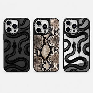 May include: Three smartphone cases with a triple-lens camera cutout. The left case is dark gray with black snake illustrations. The center case features a tan and black snakeskin pattern. The right case is light gray with black snake illustrations.