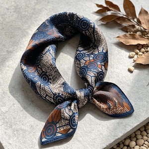 May include: A square silk scarf tied in a knot, featuring a dark blue background with intricate patterns of concentric circles and textured brown shapes. The design includes repeating circular motifs and organic lines in shades of navy and copper.