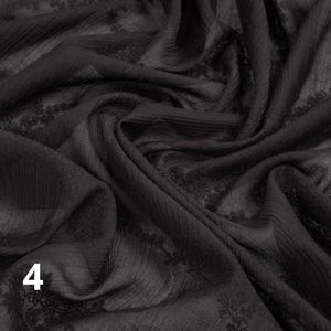 May include: Black fabric with a textured, slightly sheer appearance. The fabric has a subtle pattern and is draped in soft folds. The number "4" is visible in the lower left corner. This fabric is suitable for apparel and craft projects.