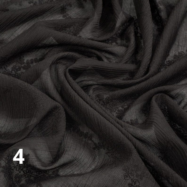 May include: Black fabric with a textured, slightly sheer appearance. The fabric has a subtle pattern and is draped in soft folds. The number "4" is visible in the lower left corner. This fabric is suitable for apparel and craft projects.