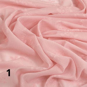 May include: A close-up of a soft, pale pink fabric with a delicate floral pattern. The fabric is draped and folded, creating shadows and texture. The number "1" is visible in the lower left corner.