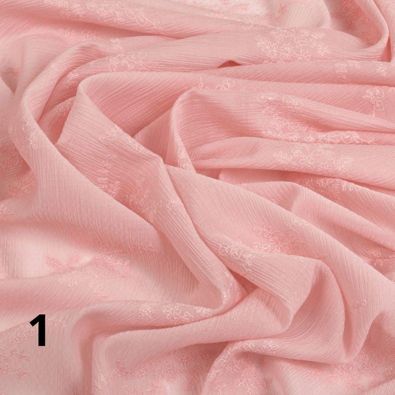 May include: A close-up of a soft, pale pink fabric with a delicate floral pattern. The fabric is draped and folded, creating shadows and texture. The number "1" is visible in the lower left corner.
