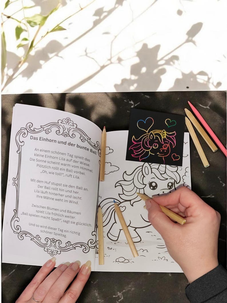 Op de afbeelding: Een kleurboek met een eenhoornthema, open op een pagina met een lijntekening van een eenhoorn. Er liggen verschillende kleurpotloden rond het boek. Een hand houdt een potlood vast en kleurt de eenhoorn in.