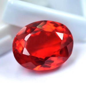 May include: A faceted, oval-shaped gemstone with a vibrant red hue. The gem's surface reflects light, showcasing its multiple facets and internal brilliance. The gemstone is a striking example of fine jewelry.