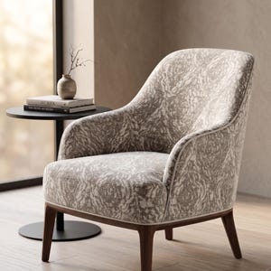 May include: A patterned armchair with a curved back and wooden legs. The chair features a light-colored fabric with a swirling design. A small side table with a vase and books is next to the chair.