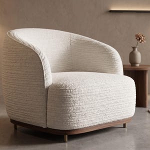 Op de afbeelding: Een crèmekleurige, tonvormige fauteuil met een textuurstof. De stoel heeft een donkere houten basis met messingkleurige poten. Een kleine houten bijzettafel en een vaas met gedroogde bloemen staan op de achtergrond.