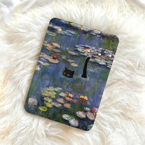 Può includere: Una custodia rettangolare con un design stravagante di un gatto nero che nuota in uno stagno con ninfee. L'opera d'arte ricorda un dipinto di Monet, con una tavolozza di colori blu e verdi.