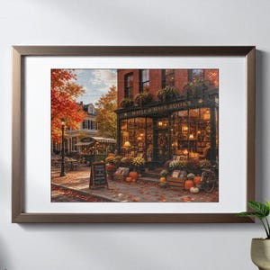 Puede incluir: Una impresi&oacute;n de arte mural enmarcada que representa una acogedora librer&iacute;a llamada Maple & Main Books durante el oto&ntilde;o. La escena presenta follaje oto&ntilde;al naranja, calabazas y una cafeter&iacute;a en la acera. La fachada tiene grandes ventanales.