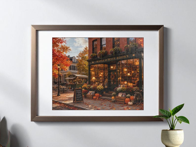 Puede incluir: Una impresi&oacute;n de arte mural enmarcada que representa una acogedora librer&iacute;a llamada Maple & Main Books durante el oto&ntilde;o. La escena presenta follaje oto&ntilde;al naranja, calabazas y una cafeter&iacute;a en la acera. La fachada tiene grandes ventanales.