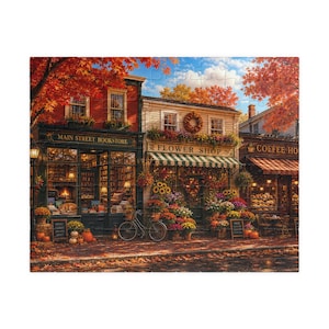 May include: A jigsaw puzzle depicting a street scene with a bookstore, flower shop, and coffee house. The buildings feature autumn foliage, pumpkins, and storefront signs reading Main Street Bookstore, Flower Shop, and Coffee House.