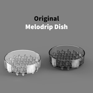 May include: Two clear, circular Melodrip dishes. The dishes have a grid-like interior design and are labeled "Original Melodrip Dish" in white text. The dishes are made of a transparent material and are set against a gray background.