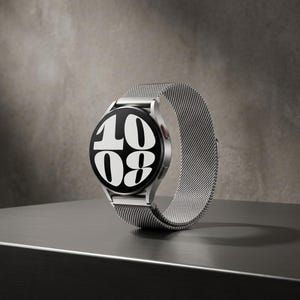 May include: A silver smartwatch with a mesh strap showing the time as 10:08. The watch has a black face with white numerals and a red button. It sits on a dark grey surface.