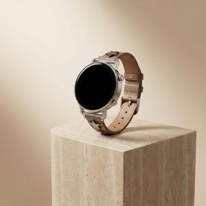 Puede incluir: Un reloj inteligente plateado con pantalla negra y correa de cuero marrón claro. La correa presenta recortes en forma de estrella. El reloj se exhibe sobre un pedestal cuadrado beige sobre un fondo neutro.