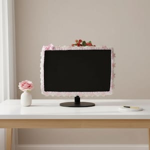 Könnte beinhalten: Ein schwarzer Computermonitor mit einer dekorativen Hülle mit weißer Spitzentrimmung und rosa Akzenten. Die Hülle ist mit einer rosa Schleife und kleinen floralen Verzierungen verziert. Eine kleine Vase mit einer rosa Rose steht auf dem Tisch.