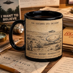 Op de afbeelding: Een zwarte keramische mok met een vintage-stijl illustratie van het Socorro UFO-incident. Het ontwerp toont een schotelvormig vaartuig, een politieauto en een figuur, met de tekst THE SOCORRO UFO INCIDENT en OFFICIAL REPORT REPRODUCTION.