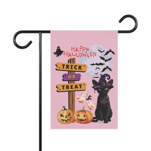 Peut inclure: Un drapeau de jardin rose illustré d'un chat noir portant un chapeau de sorcière violet, deux citrouilles d'Halloween orange et un panneau en bois avec le texte "HAPPY HALLOWEEN" et "TRICK OR TREAT". Le motif inclut une pleine lune, des chauves-souris et des petits fantômes.