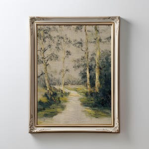 May include: An oil painting of a forest scene with a path leading through the trees. The artwork is framed in a decorative, off-white frame with gold accents. The painting features a muted color palette of greens, browns, and grays.