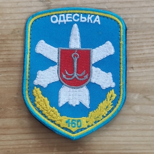 May include: A shield-shaped embroidered patch with a blue background and a yellow border. It features a white missile graphic, a red shield with a grey anchor, and yellow wheat stalks at the bottom with the number 160 and the text ODESKA in white.