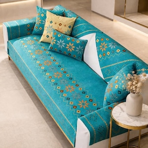 May include: A turquoise sofa cover with a floral and geometric pattern. The cover features a repeating design of orange and blue flowers and diamonds. Several throw pillows in matching colors and patterns are arranged on the sofa.